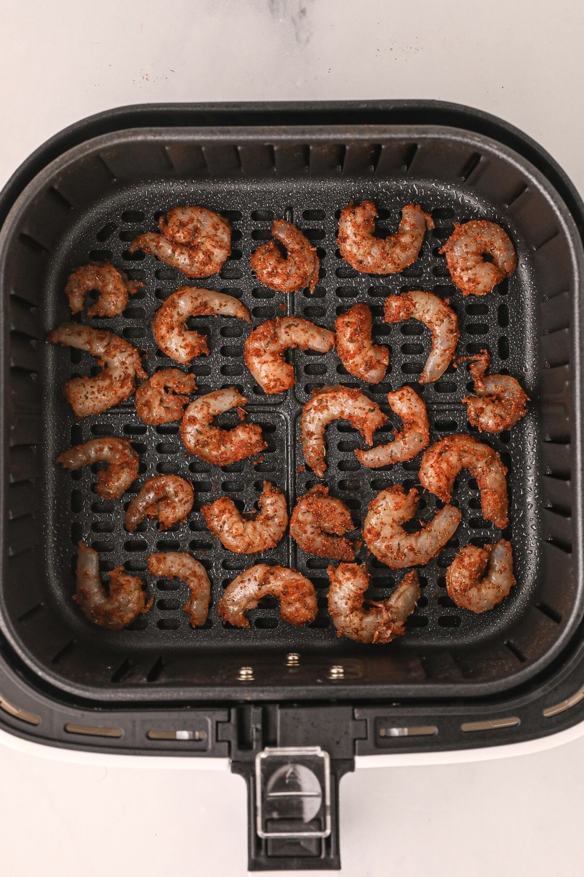 Seasoned shrimp in the air fryer basket before being cooked in the air fryer