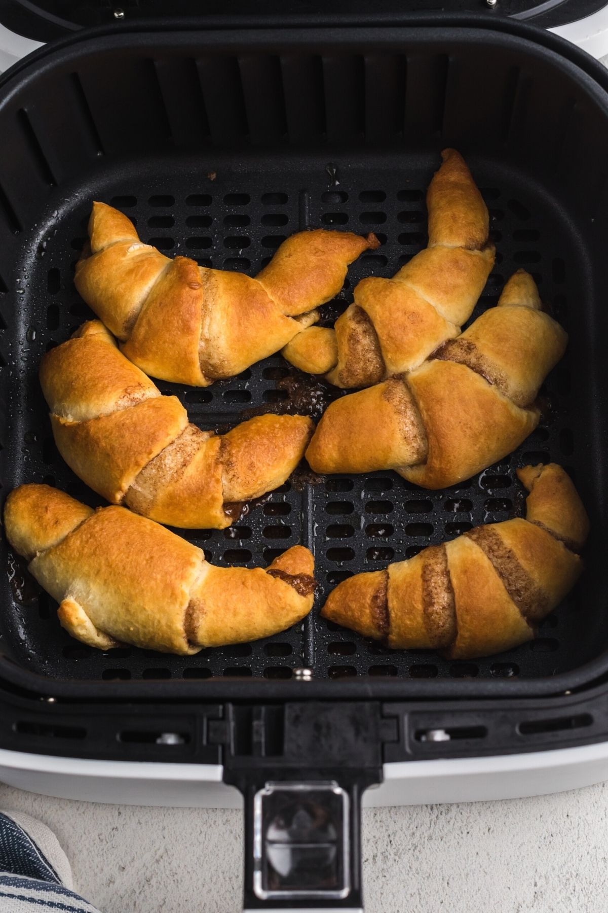 Golden cooked crescent rolls with cinnamon mixture mixed in each roll, in the air fryer basket