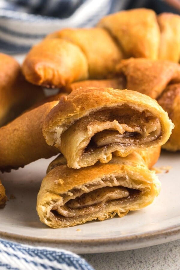 Golden filled crescent rolls on a white plate showing one cut in half with cinnamon mixture in the center