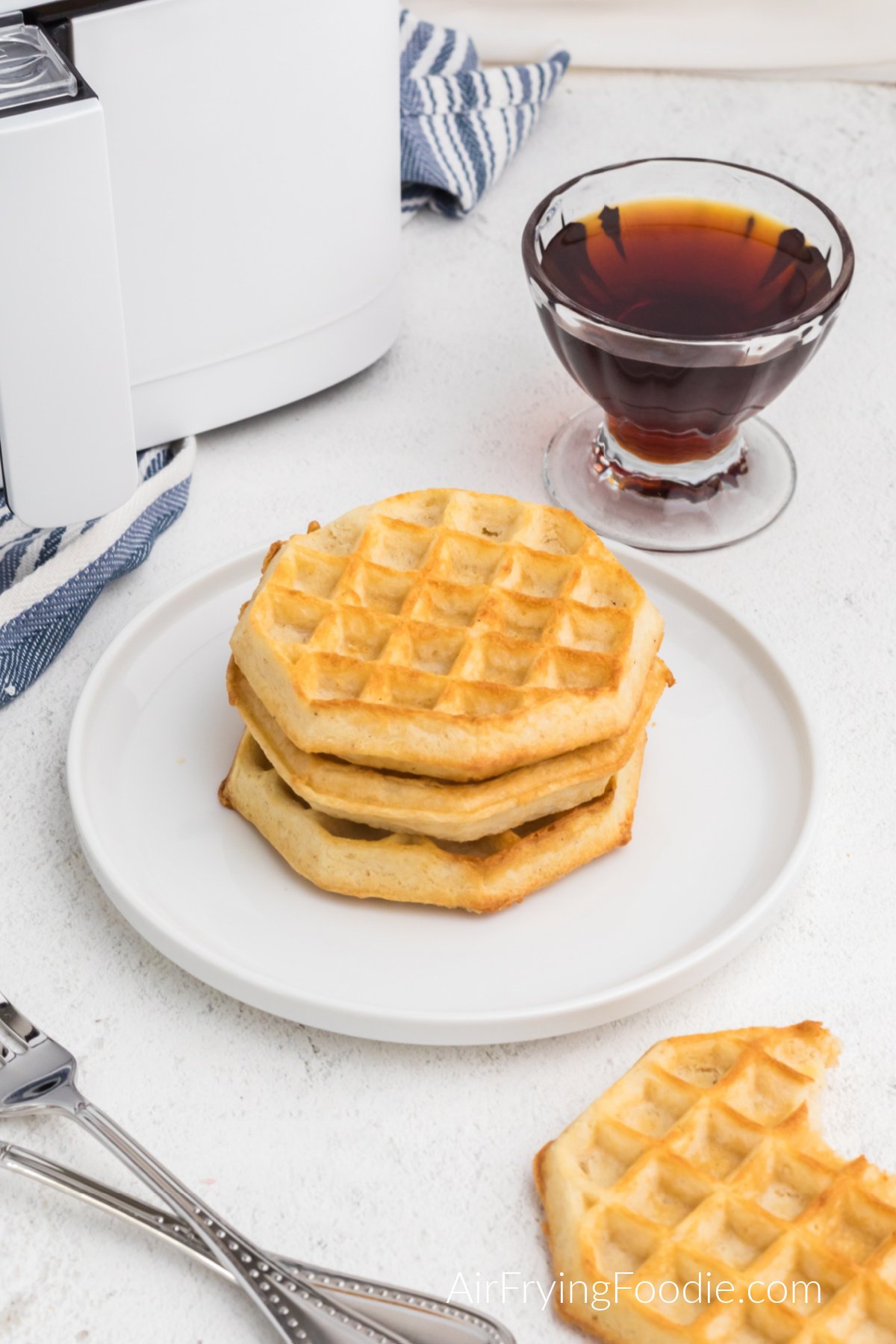 Air fried waffled made from frozen on a plate and one on the table that is missing a bite.