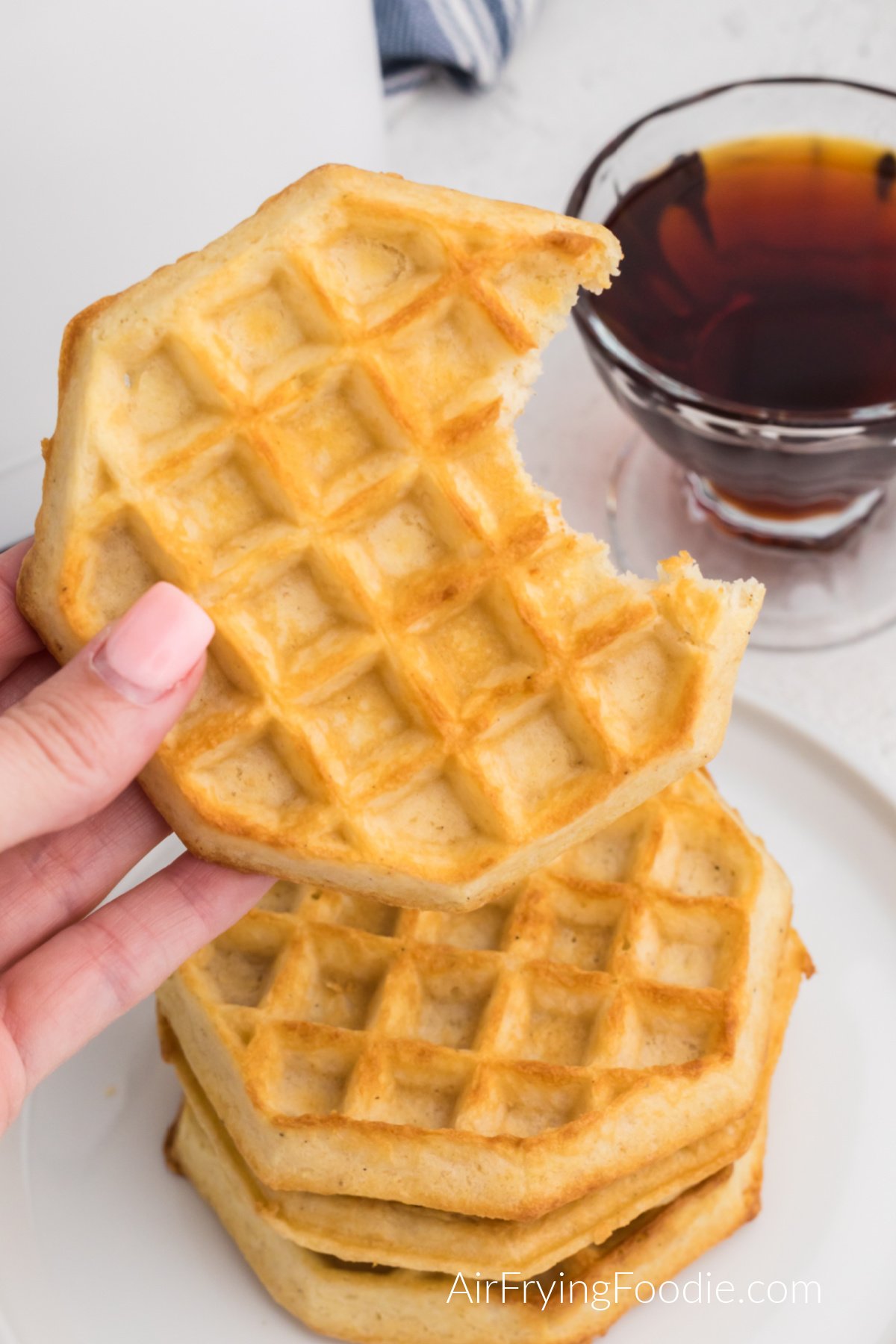 Close up of frozen waffles fully cooked in the air fryer, with a hand holding one that's missing a bite.