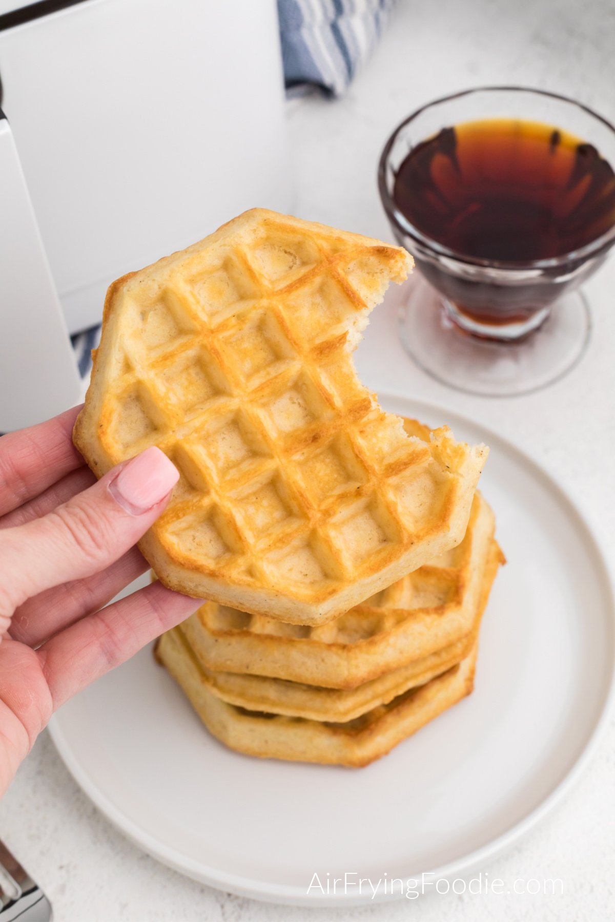 Waffles made in the air fryer from frozen, stacked on a plate, with a hand holding one that is missing a bite.