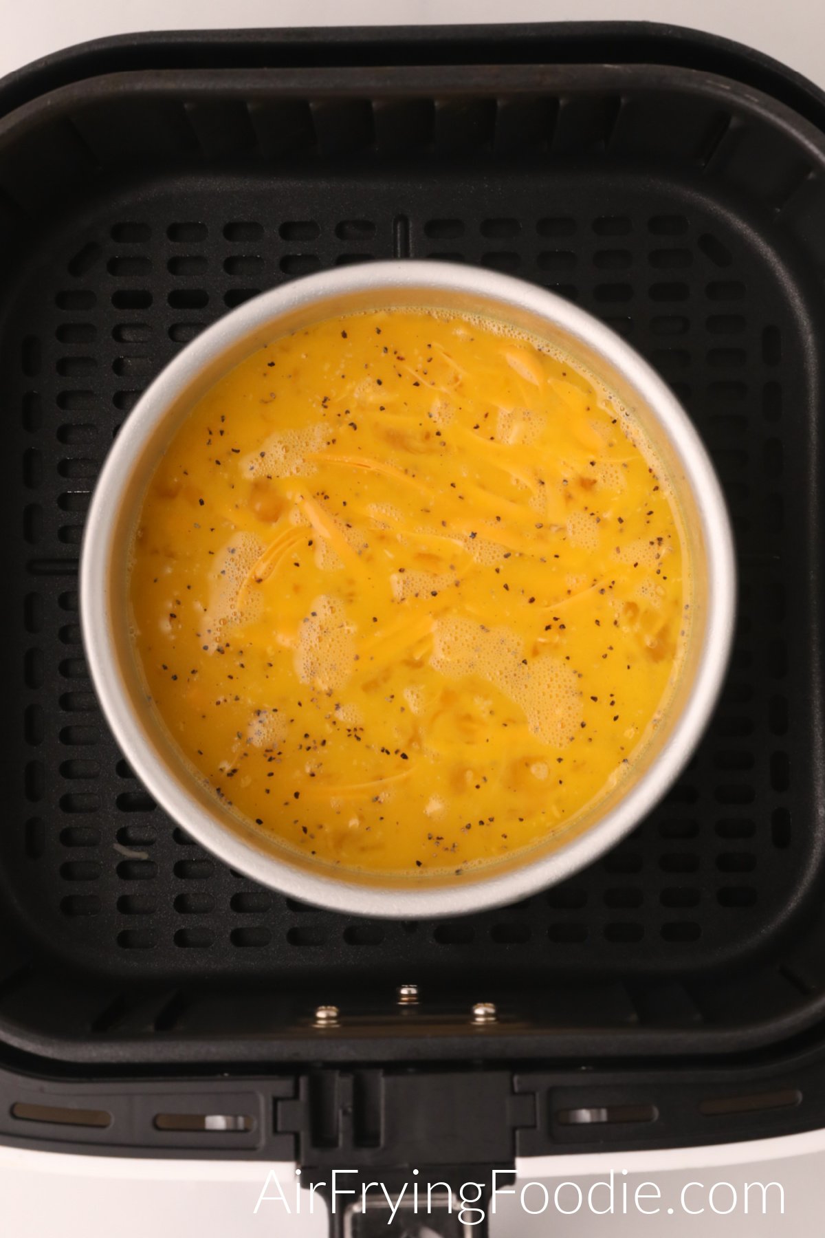 Whisked eggs and cheese in a bowl in the basket of the air fryer.