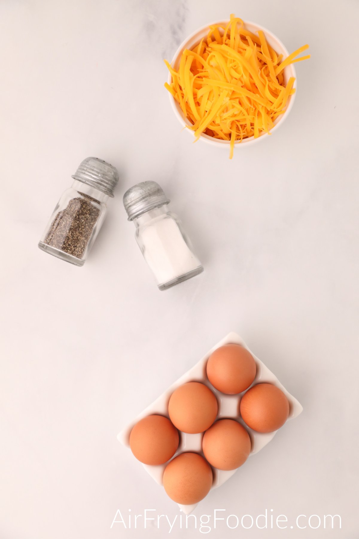 Ingredients needed to make scrambled eggs in the air fryer - cheese in a bowl, salt and pepper, and eggs. 