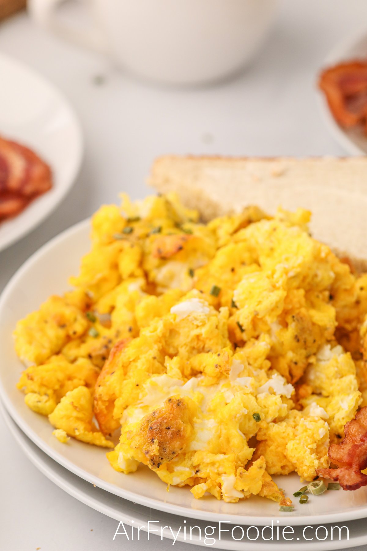 Scrambled eggs that were made in the air fryer on a plate with bacon and toast. 