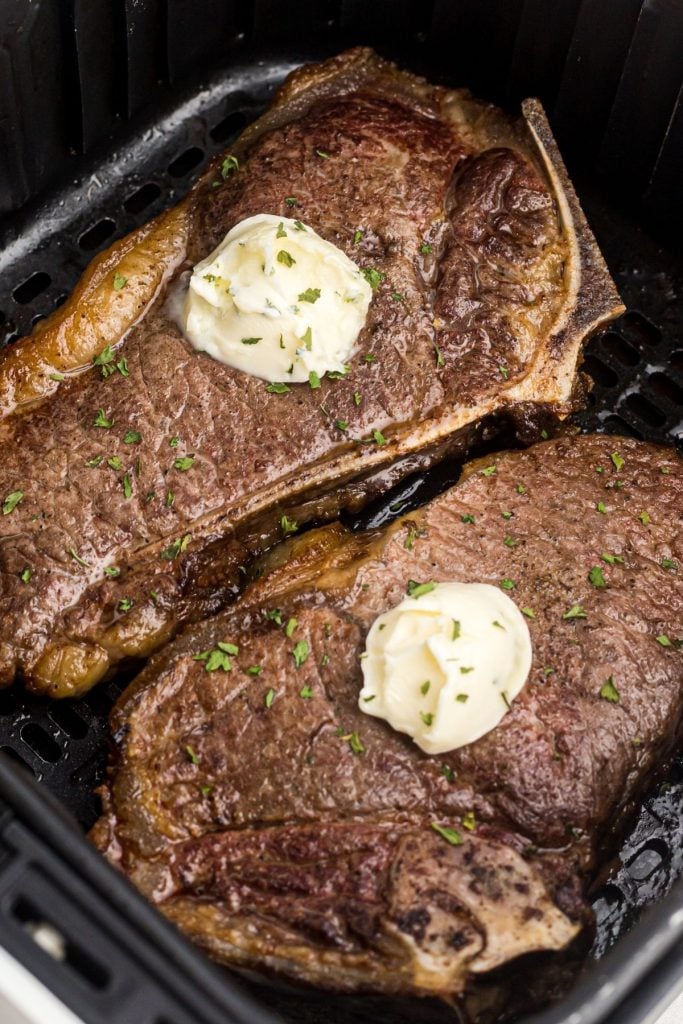 Close up of juicy steaks in the air fryer basket with butter and parsley flakes