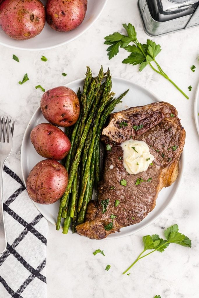 Juicy steak on a white plate with asparagus and red potatoes. 