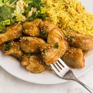 Close up fork shot of sweet and sour chicken served on a white plate with rice and salad