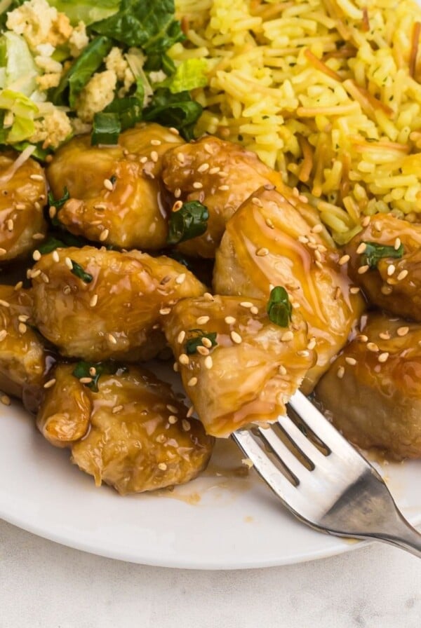 Close up fork shot of sweet and sour chicken served on a white plate with rice and salad