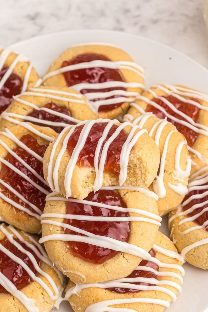 Close up photo of thumbprint cookies with strawberry jam on top drizzled with melted white chocolate