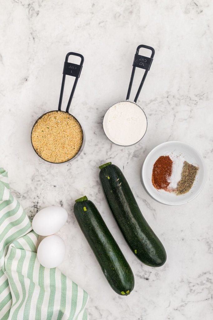 Ingredients needed to make zucchini chips measured on a white marble talbe