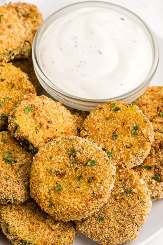 Crispy golden zucchini chips on a white plate with dipping sauce