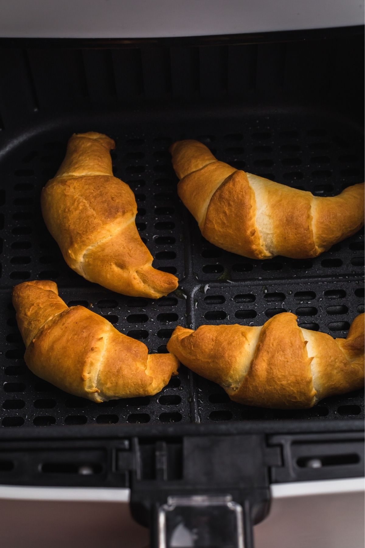 Golden croissants in the air fryer basket after being filled with chocolate and cooked