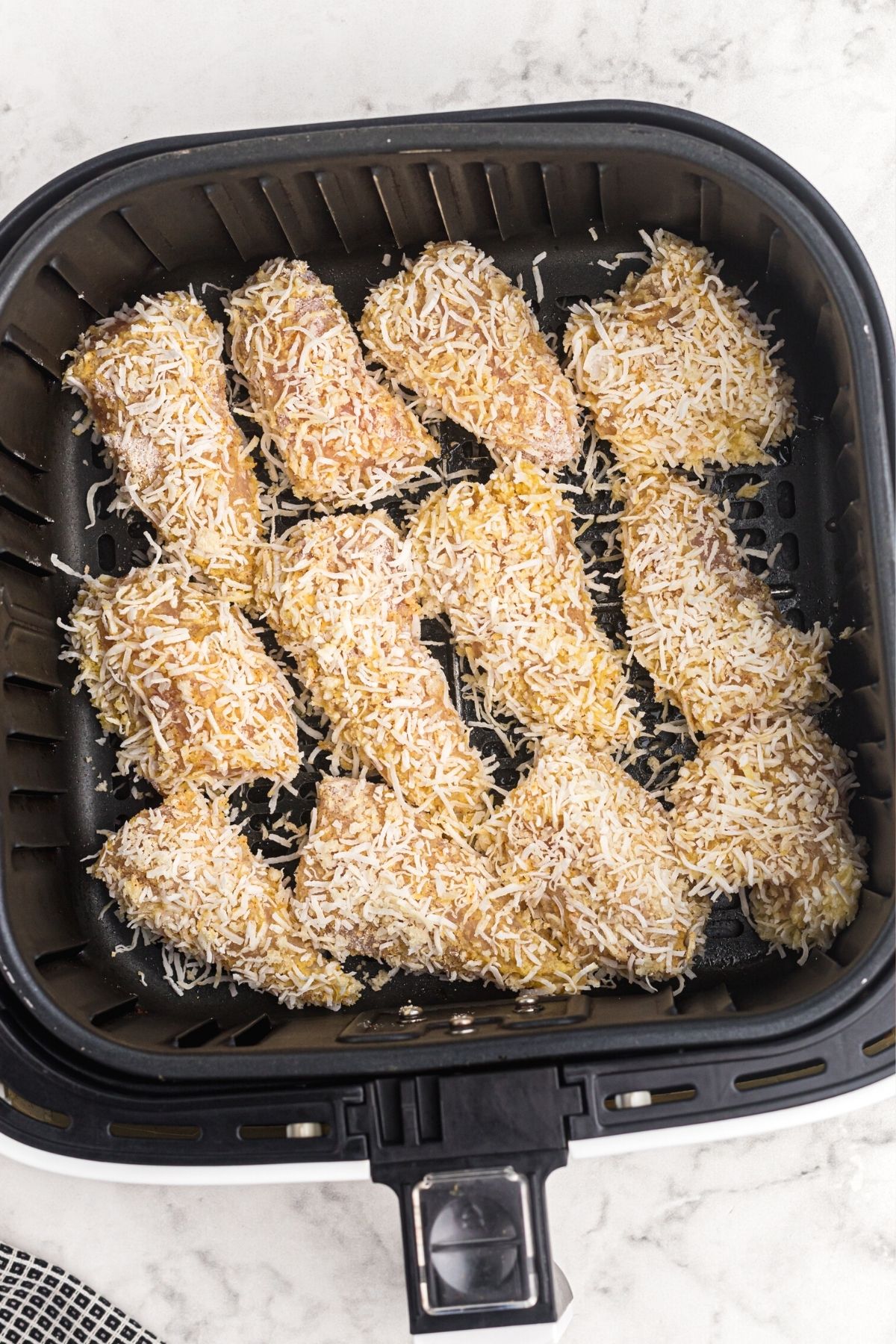 coconut crusted chicken pieces placed in the air fryer basket before being cooked