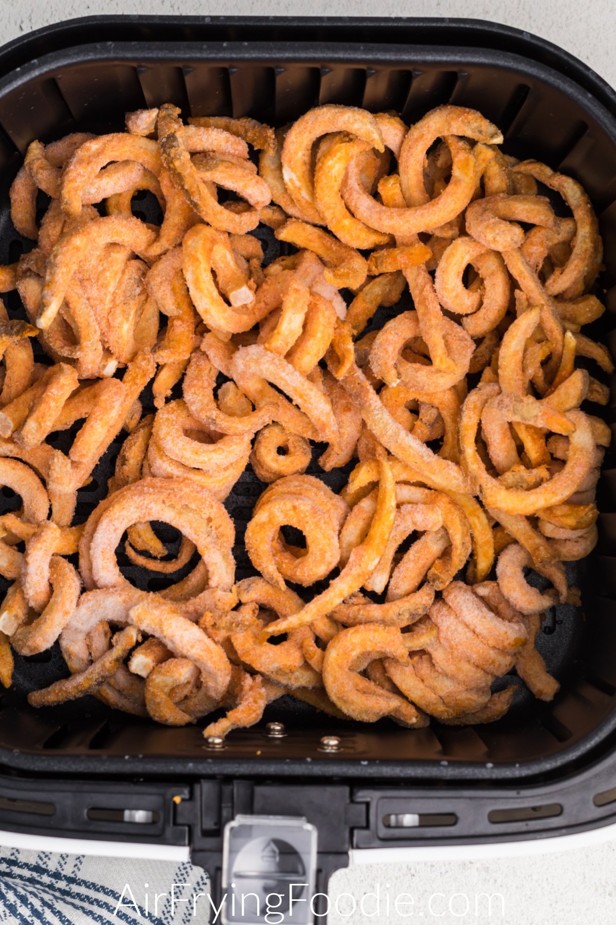 frozen curly fries in air fryer basket.