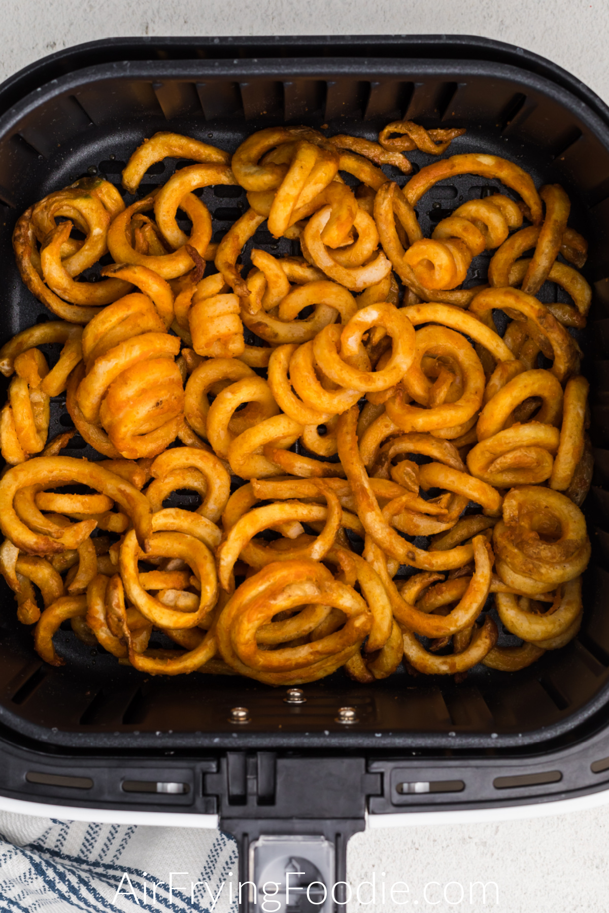 Cooked and crispy curly fries in air fryer basket, ready to serve.
