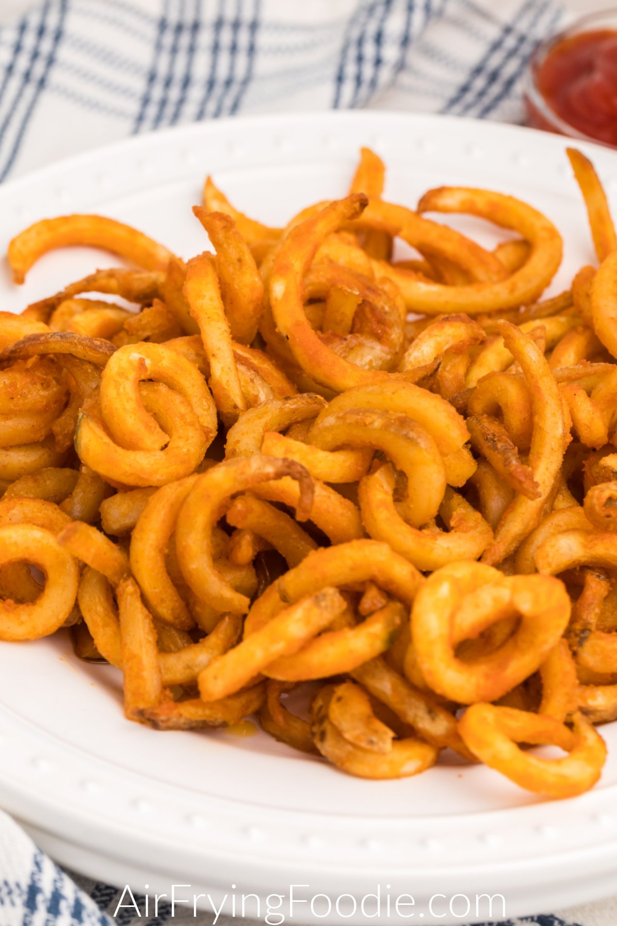 Close up of curly fries on a white plate that were made in the air fryer. 