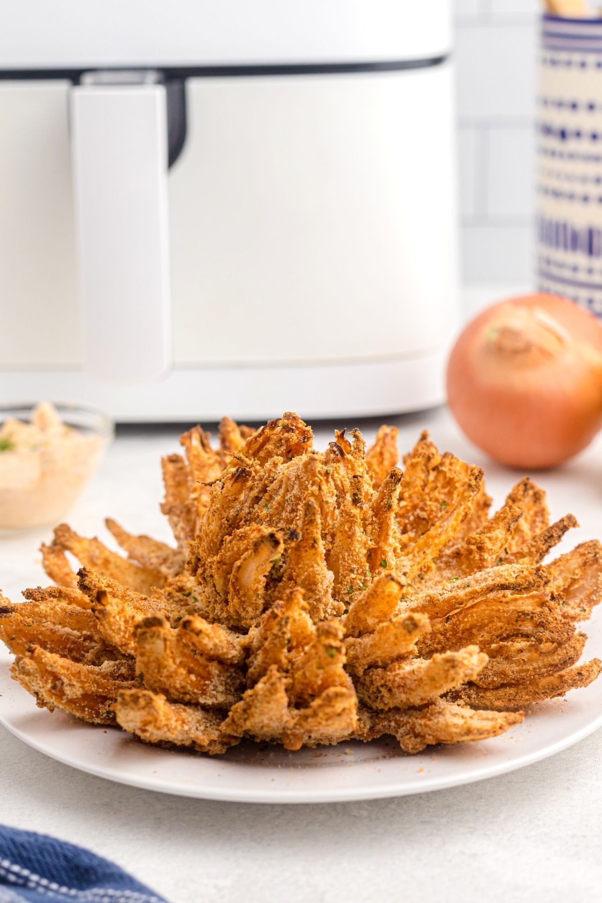 Crispy Air Fryer Blooming Onion 2 Golden crispy onion sliced open on a white plate with a side of dipping sauce