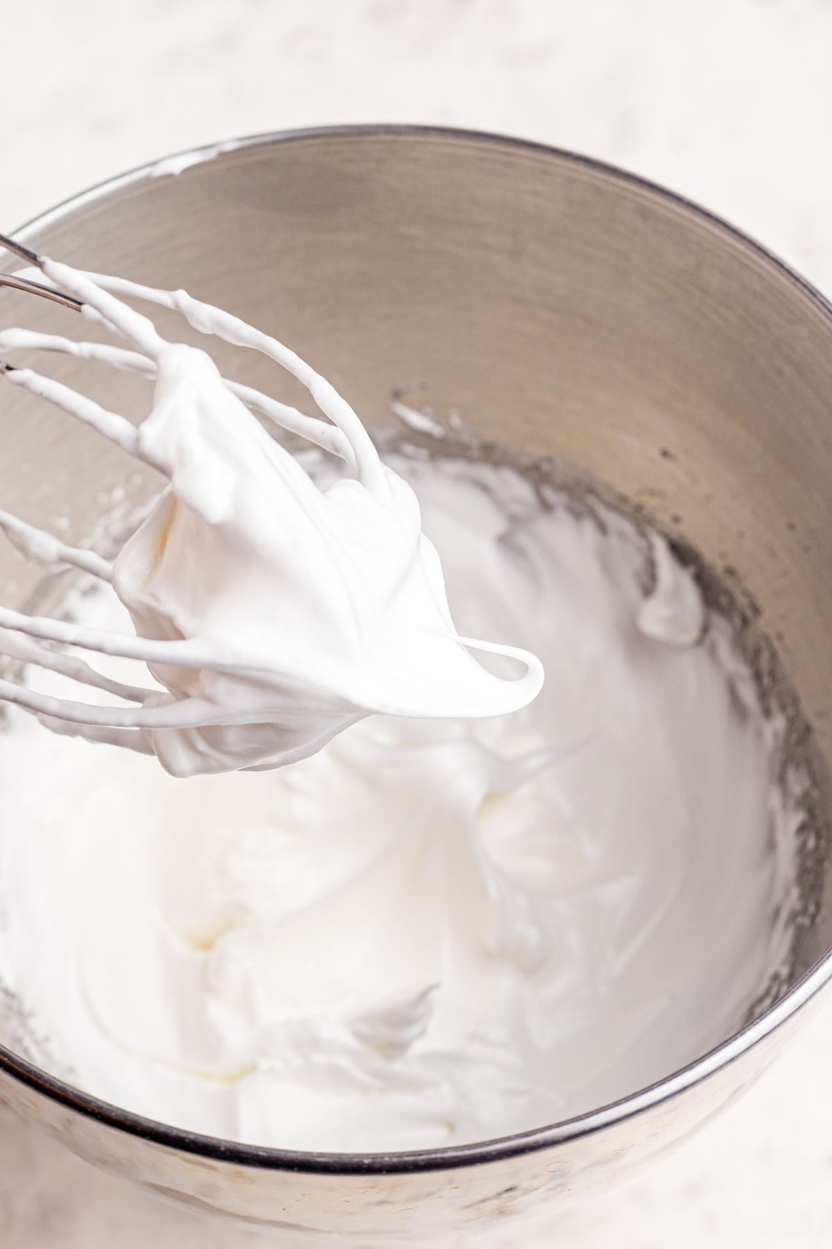 Meringue beaten into glossy peaks on a wire whisk over a mixing bowl
