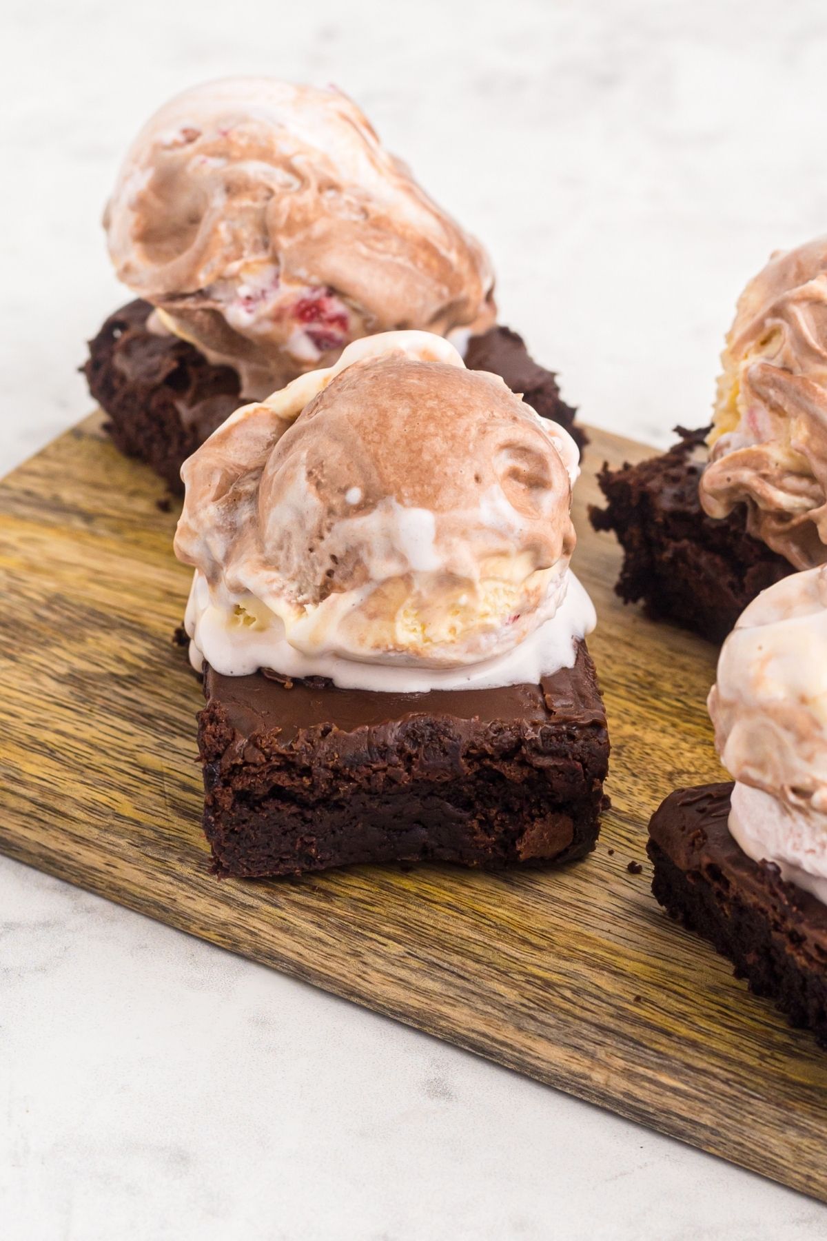 ice cream scooped onto brownies on a wooden cutting board