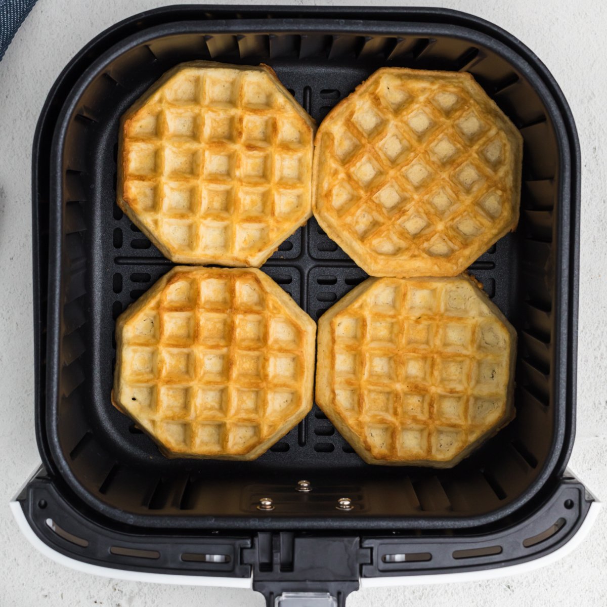 Fully cooked frozen waffles in air fryer basket in a single layer.