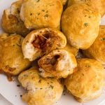 Golden biscuits filled with pizza toppings stacked on a white plate