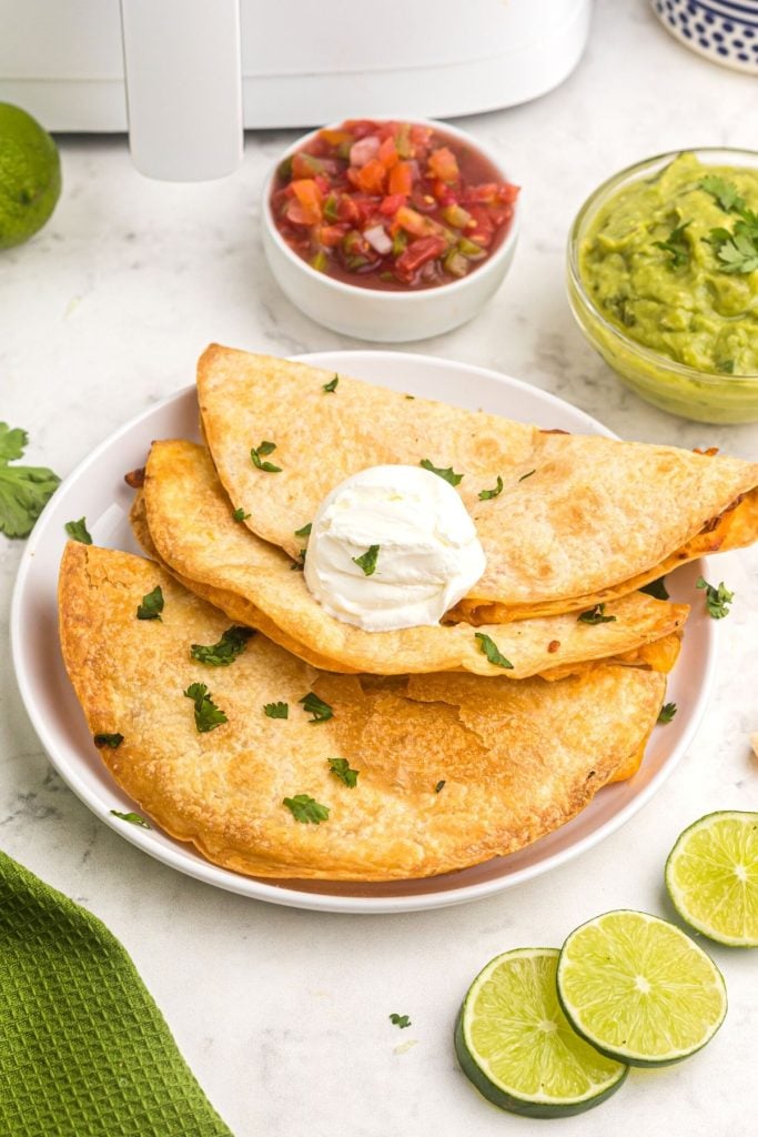 Golden crispy cheese quesadillas on a white plate with guacamole and salsa
