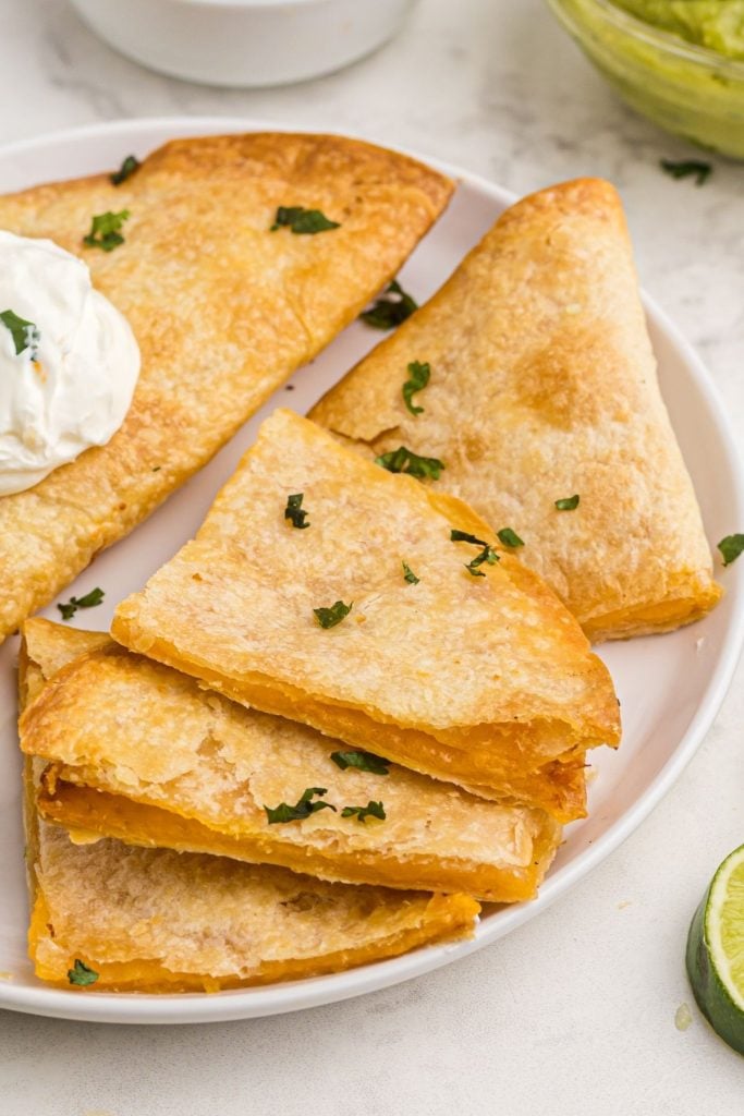Golden quesadillas filled with cheese and garnished with chopped cilantro and served with sour cream
