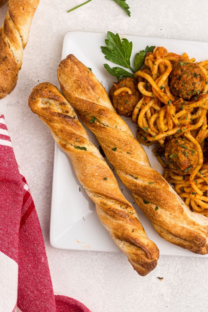 Golden breadsticks on a white plate with spaghetti and meatballs 