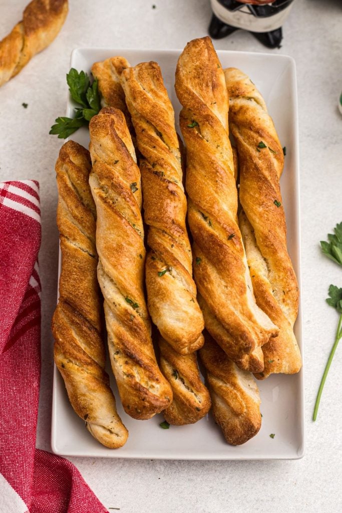 Golden Breadsticks on a white plate with a red linen and garnish with parsley flakes.