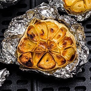 Golden roasted garlic on a piece of foil in the air fryer basket.