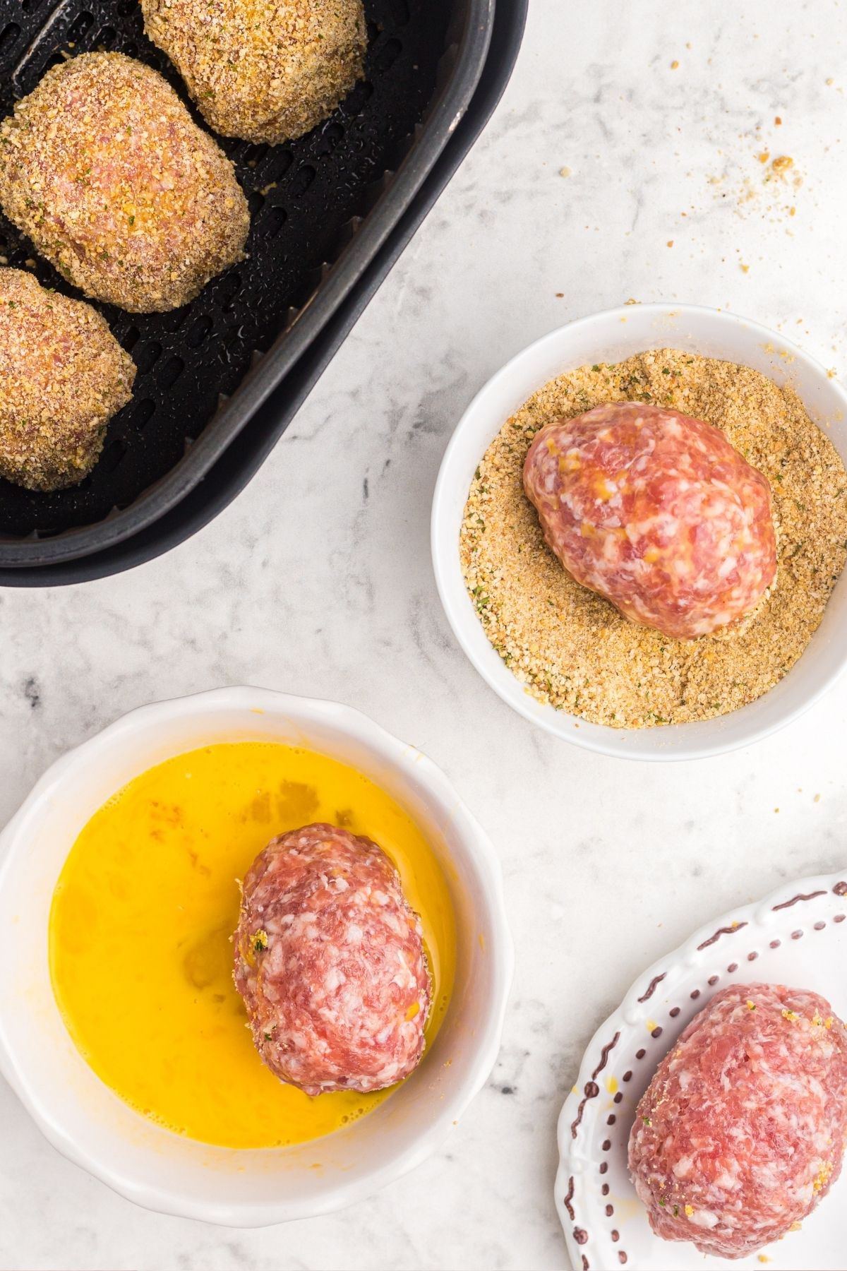 Hard boiled eggs wrapped in pork sausage and dipped in eggs with breadcrumbs and then placed in the air fryer basket