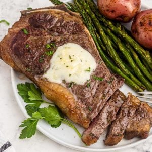 Juicy garlic on a white plate with asparagus and potatoes, the steak is sliced with a fork