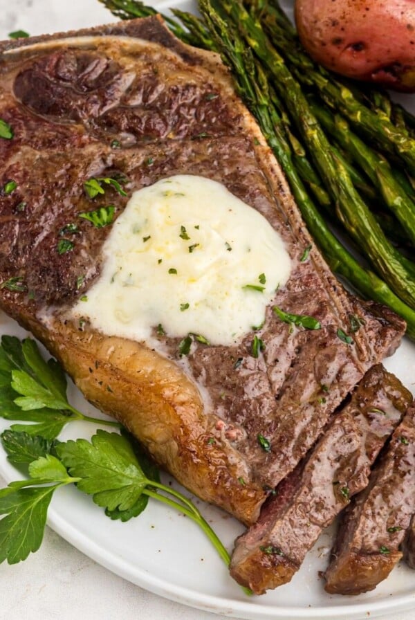 Juicy garlic on a white plate with asparagus and potatoes, the steak is sliced with a fork