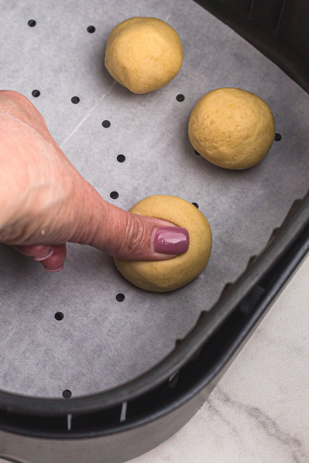 Cookie dough rolled in the air fryer basket and then a thumb pushing into dough to make a well