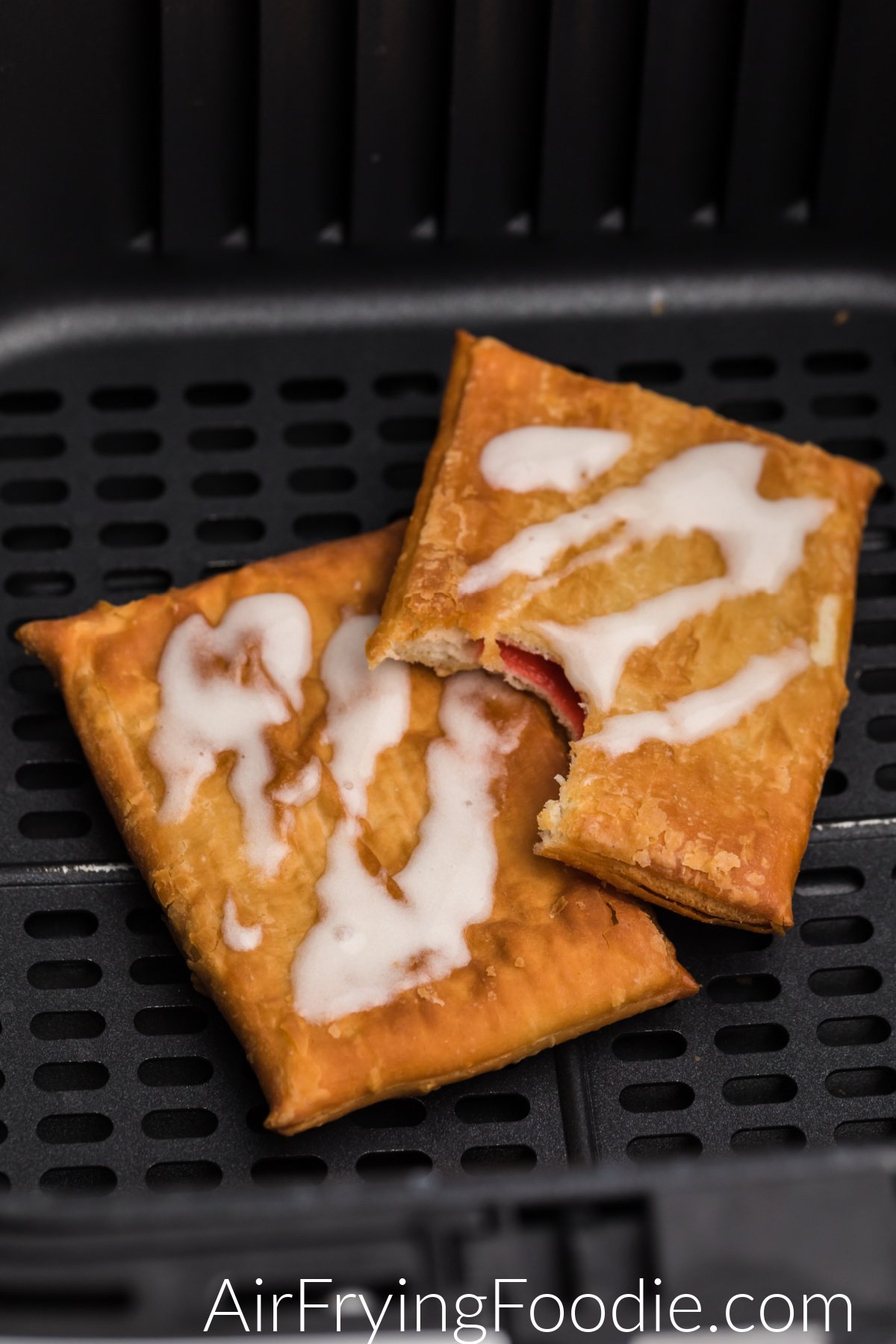 Toaster strudel in air fryer basket with frosting, and one missing a bite. 