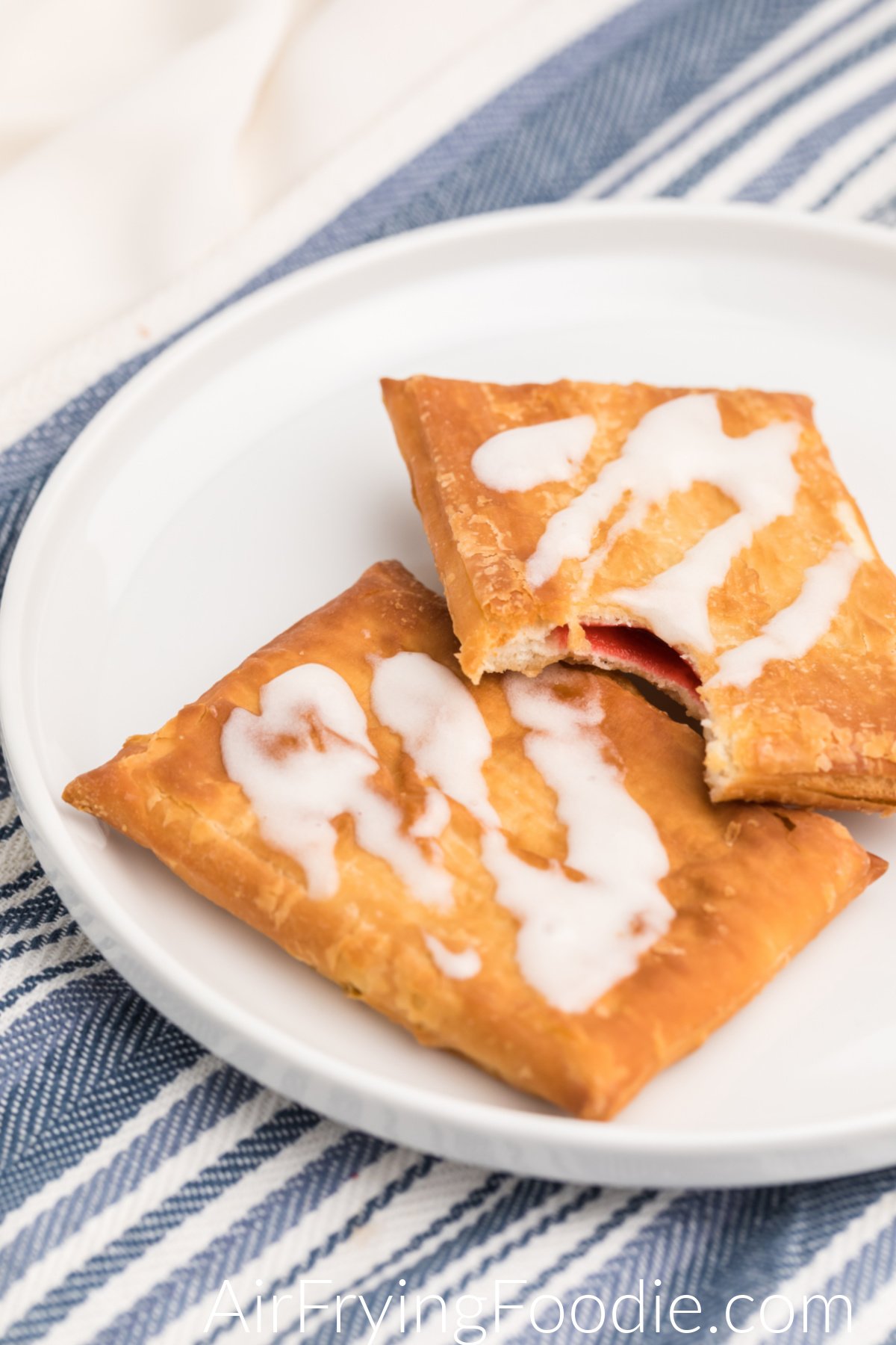 Toaster Strudel made in the air fryer and topped with frosting, served on a white plate. One strudel is missing a bite. 