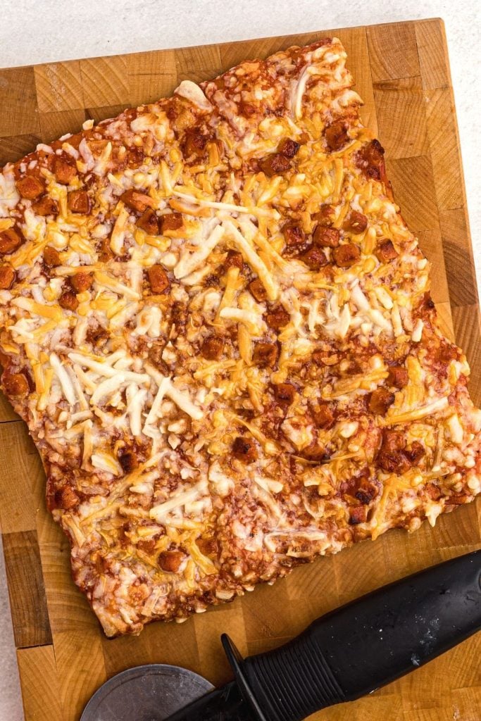 Golden crispy pizza on a cutting board with a pizza cutter on the board