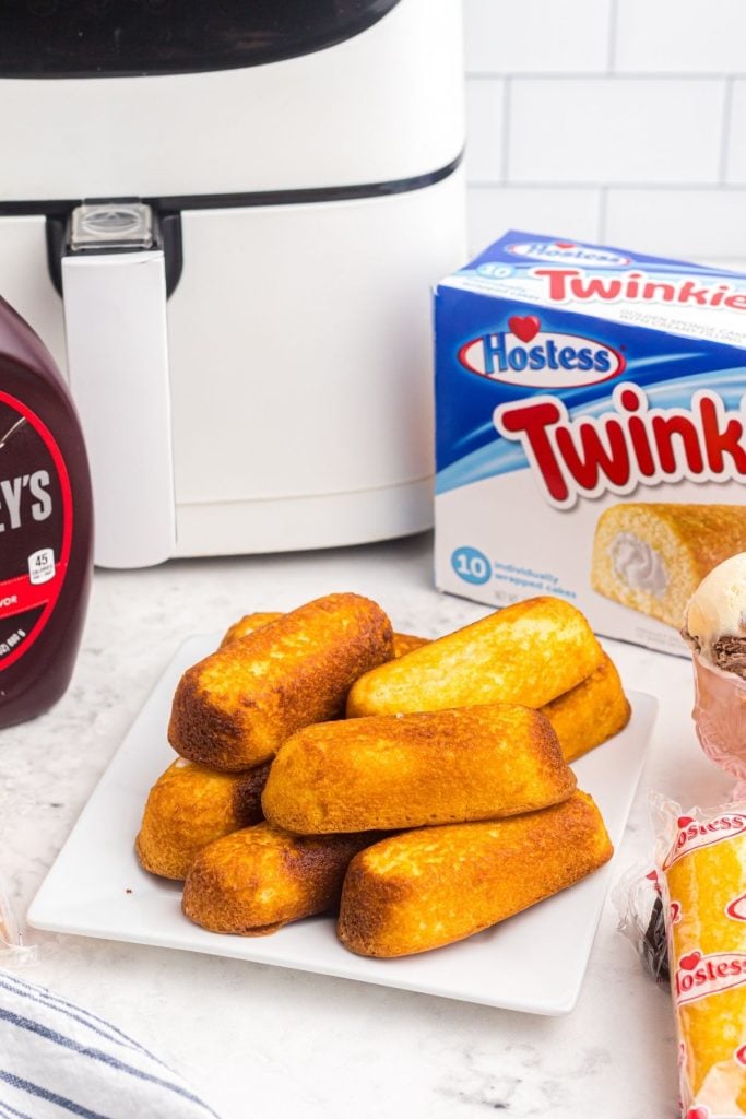 Golden crispy twinkies on a white plate with air fryer in background