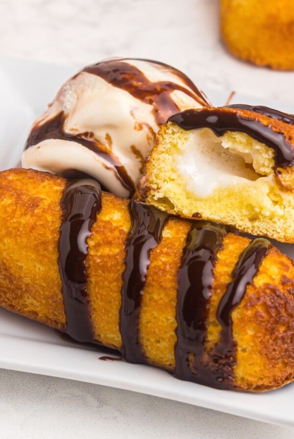 Golden crispy twinkie on a white plate served with ice cream and drizzled with chocolate sauce