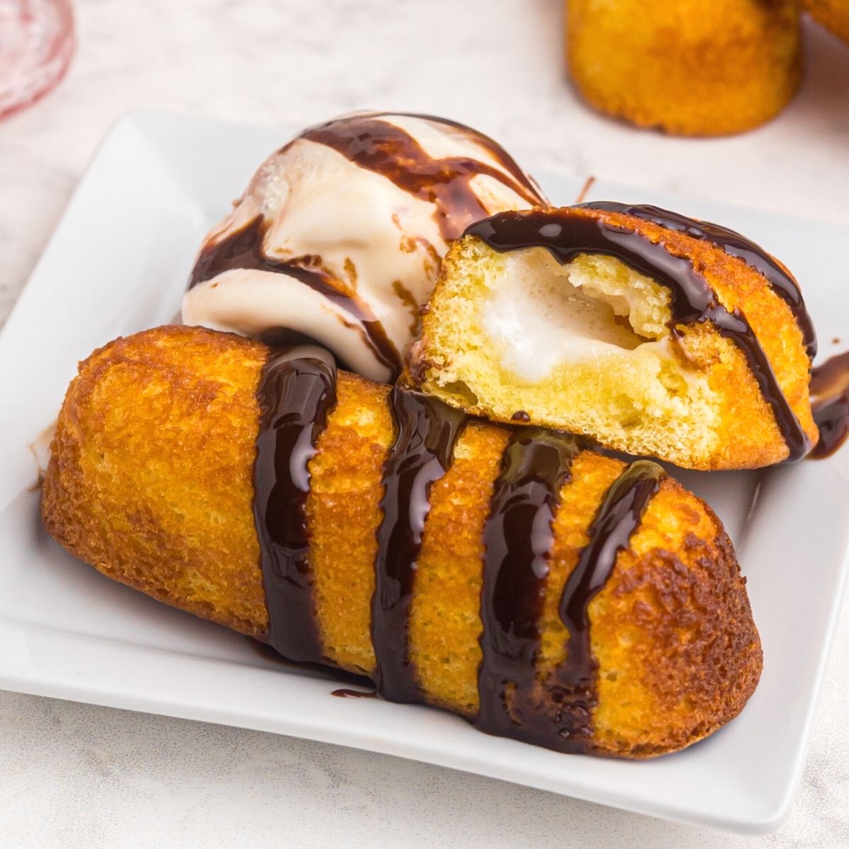 Golden crispy twinkie on a white plate served with ice cream and drizzled with chocolate sauce