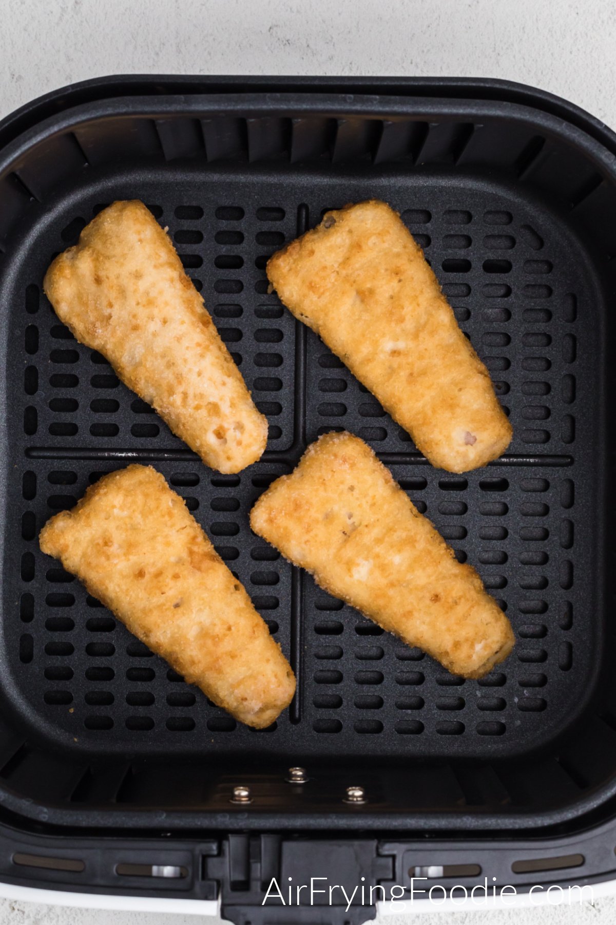 Frozen fish fillets in air fryer basket, ready to cook.