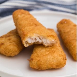 Frozen fish fillets made in the air fryer, fully cooked, and served on a white plate. One is missing a bite.