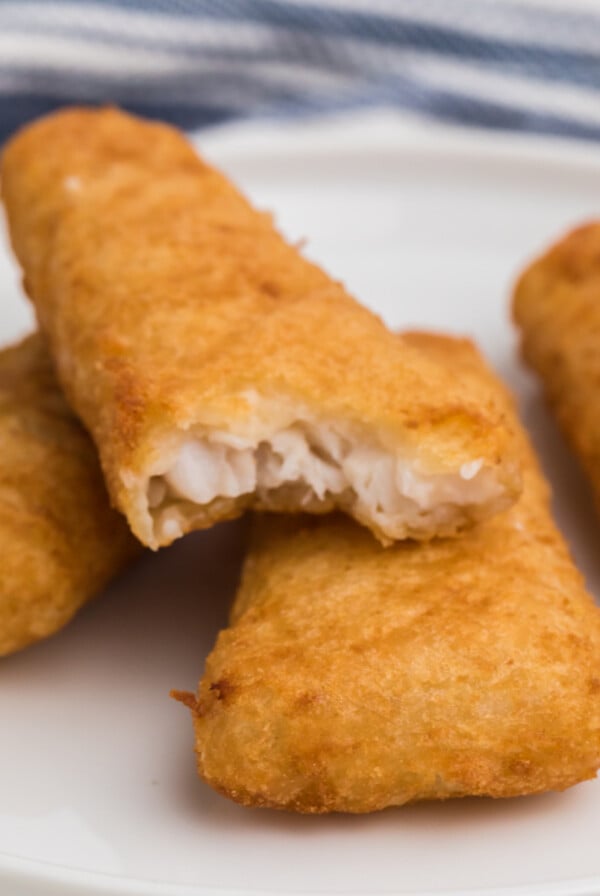 Frozen fish fillets made in the air fryer, fully cooked, and served on a white plate. One is missing a bite.