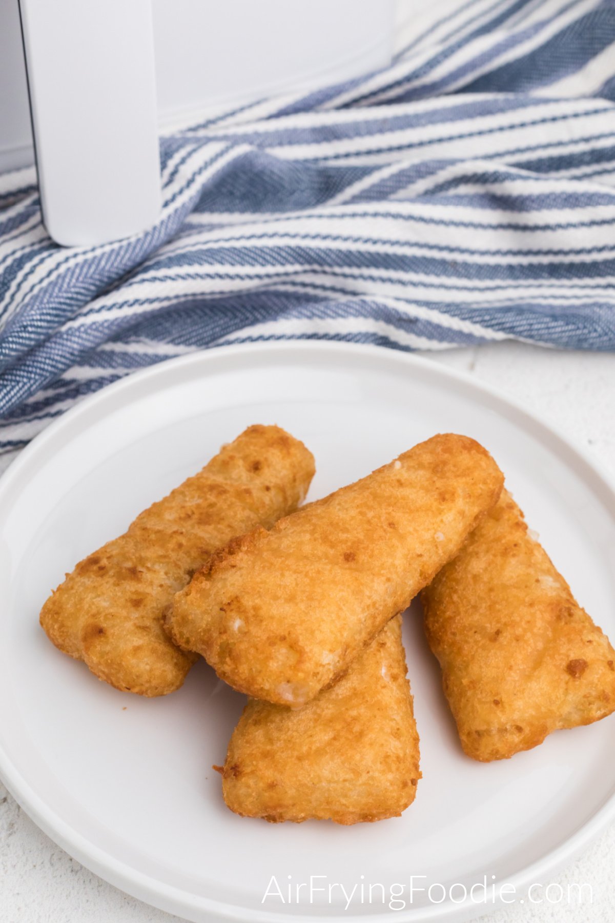 Frozen fish fillets made in the air fryer, fully cooked, and served on a white plate.