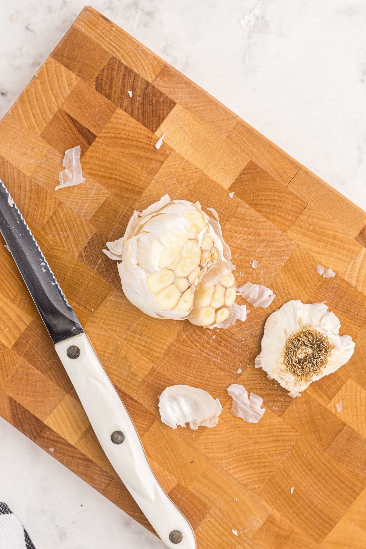 Garlic bulb with top cut off on a wooden cutting board