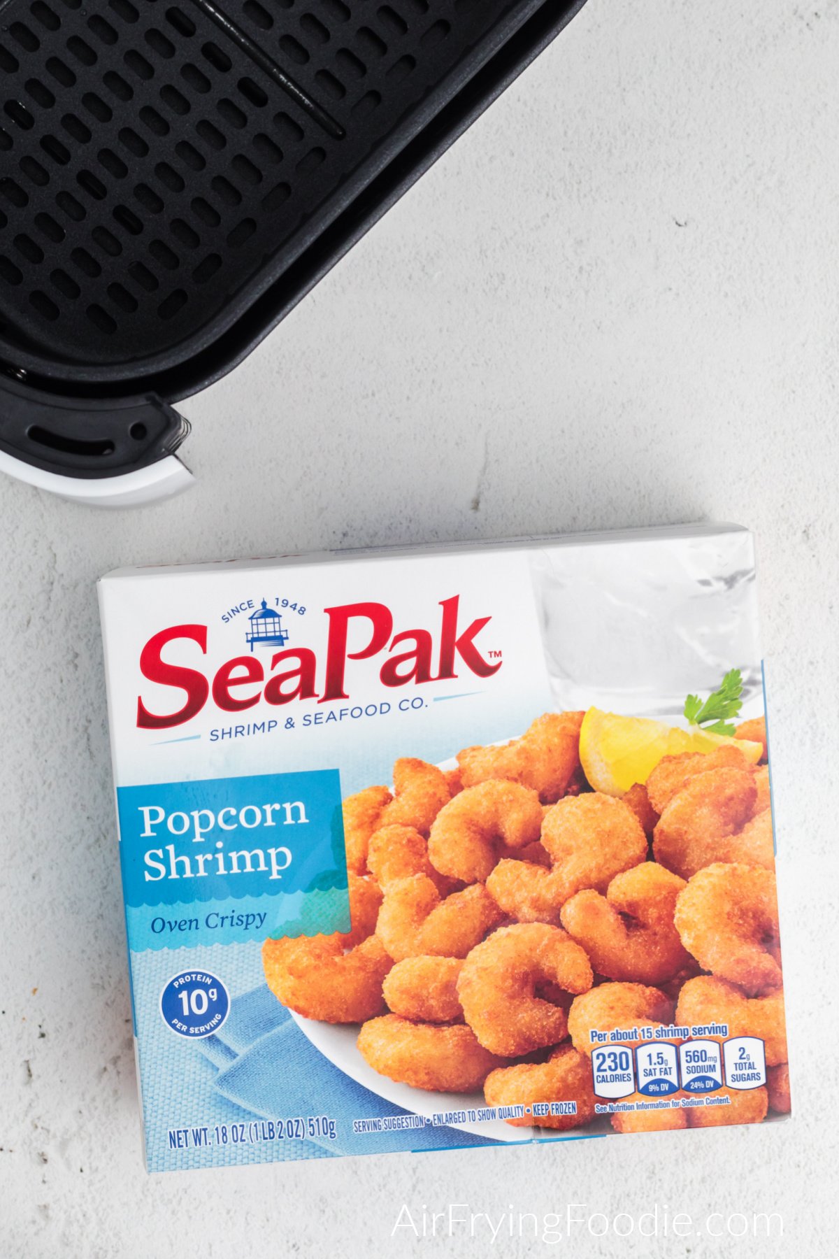 Seapak frozen popcorn shrimp and the basket of the air fryer on a white table.