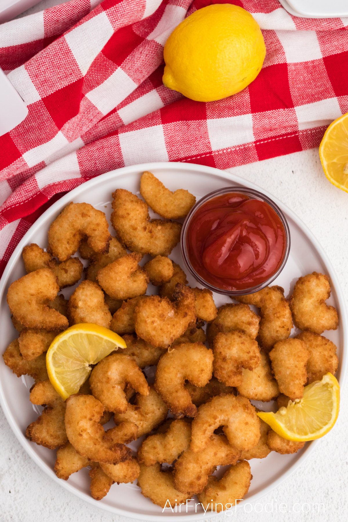 Overhead shot of popcorn shrimp made from frozen in the air fryer and served on a white plate with lemon wedges and dipping sauce. 