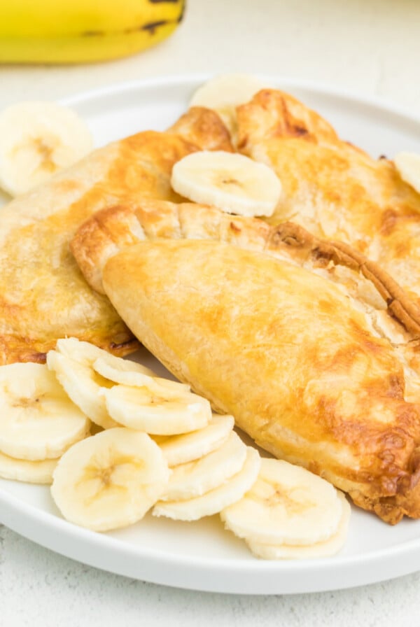 Air fried banana pudding pies on a white plate with sliced bananas.