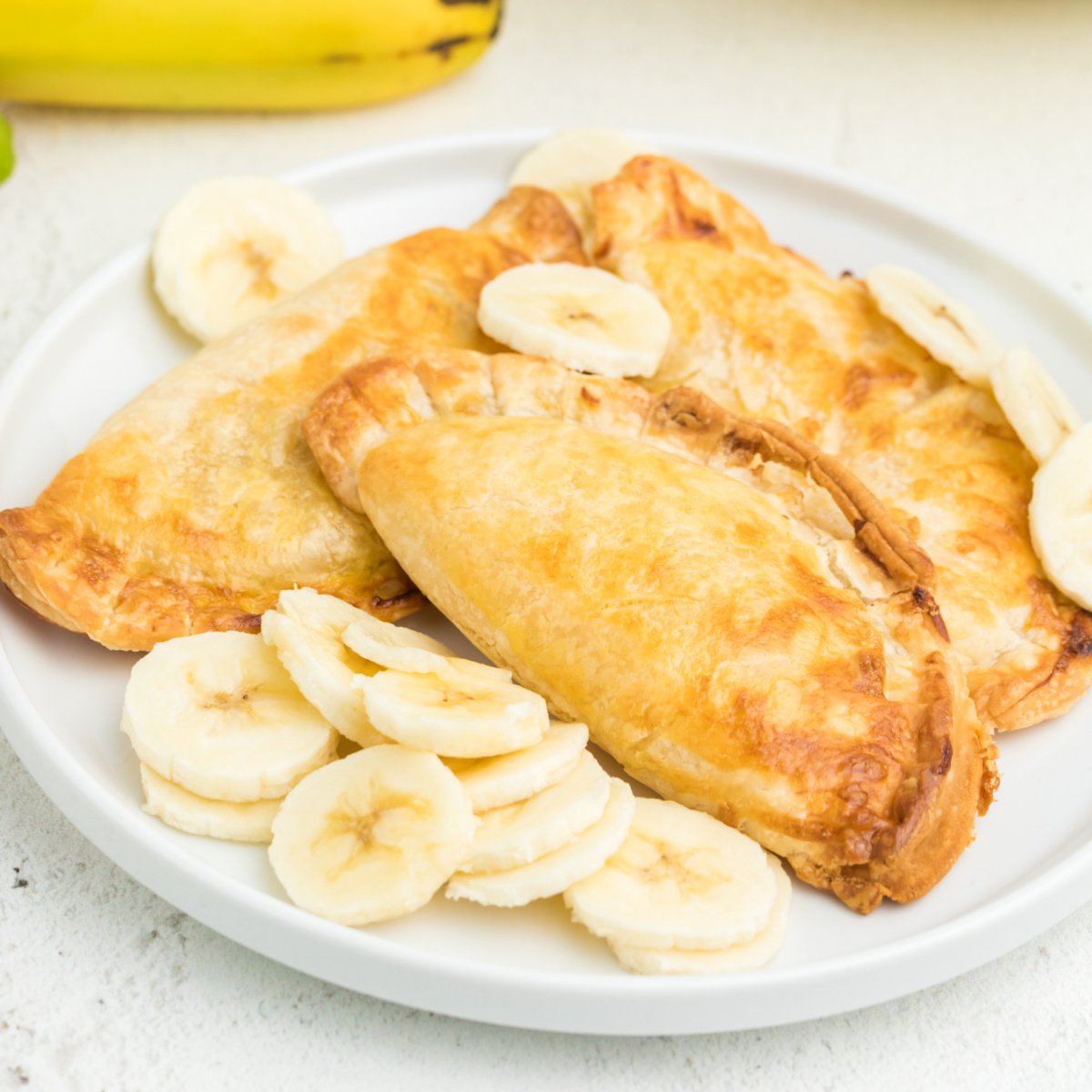 Air fried banana pudding pies on a white plate with sliced bananas.